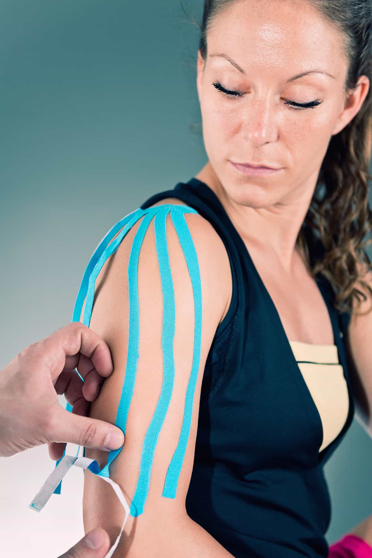 Frau bekommt blaues Kinesio Tape auf die Schulter