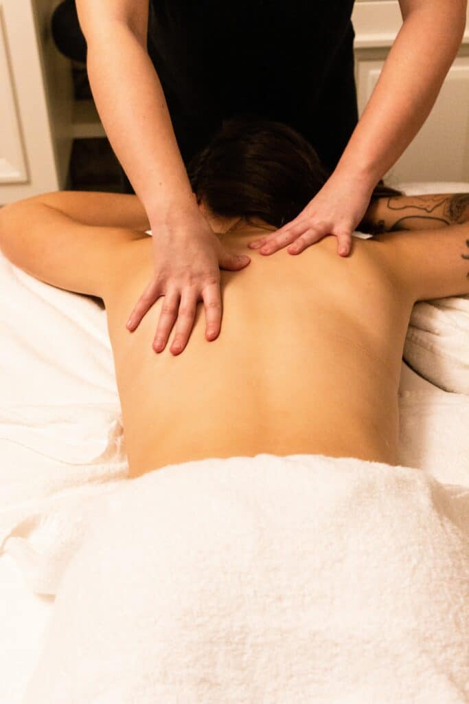 Frau auf Massageliege mit Handtuch über Popo. Wird am Rücken massiert.