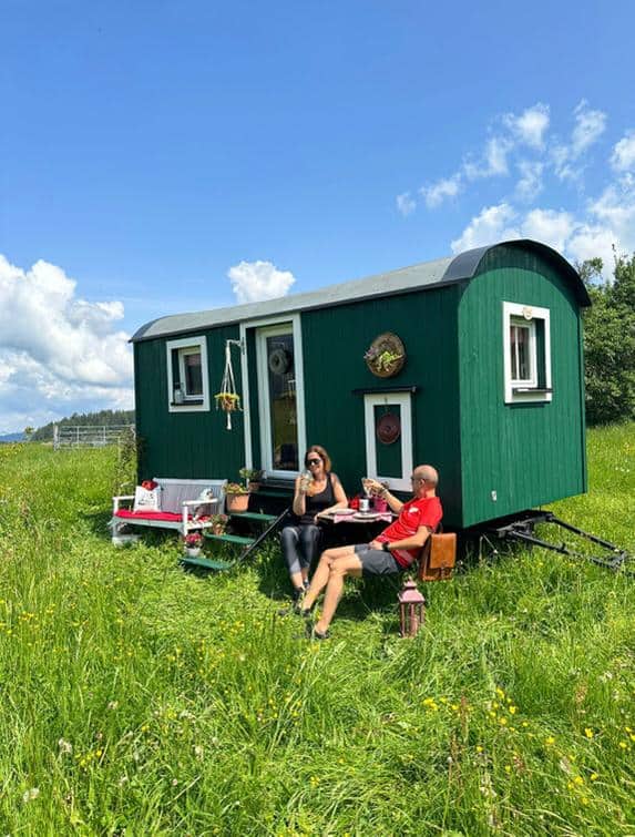 Grünes Häuschen auf Wiese mit Personen die davor sitzen